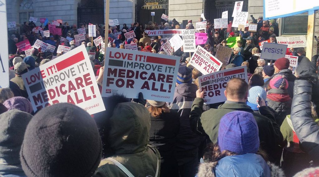 Crowd of people with "Love It! Improve It! Medicare for All!" signs