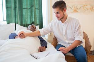 Young man holding the hand of an older man laying in bed